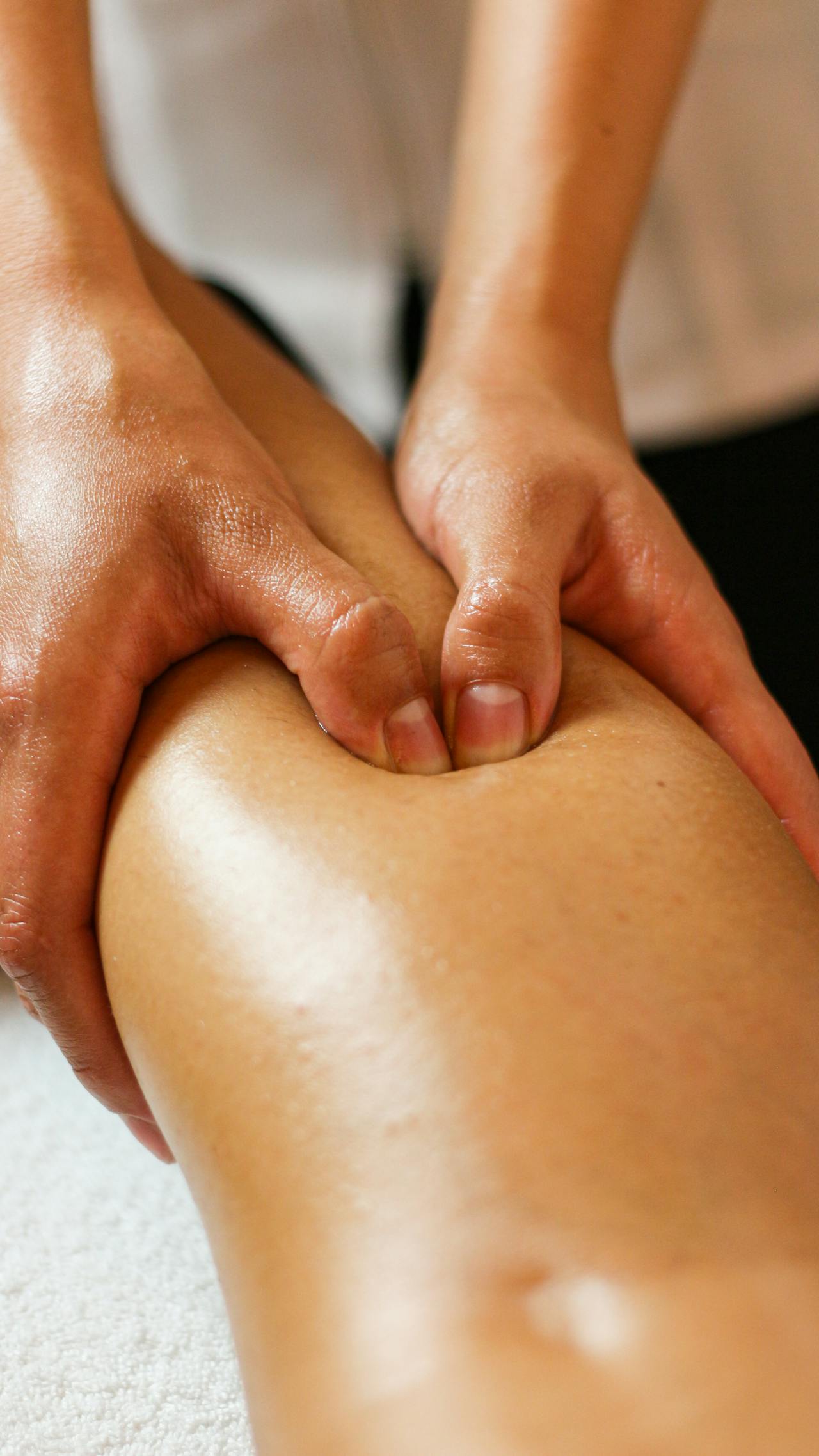 Close-up of a therapist's hands performing a kneading Swedish massage session technique on a client's leg.