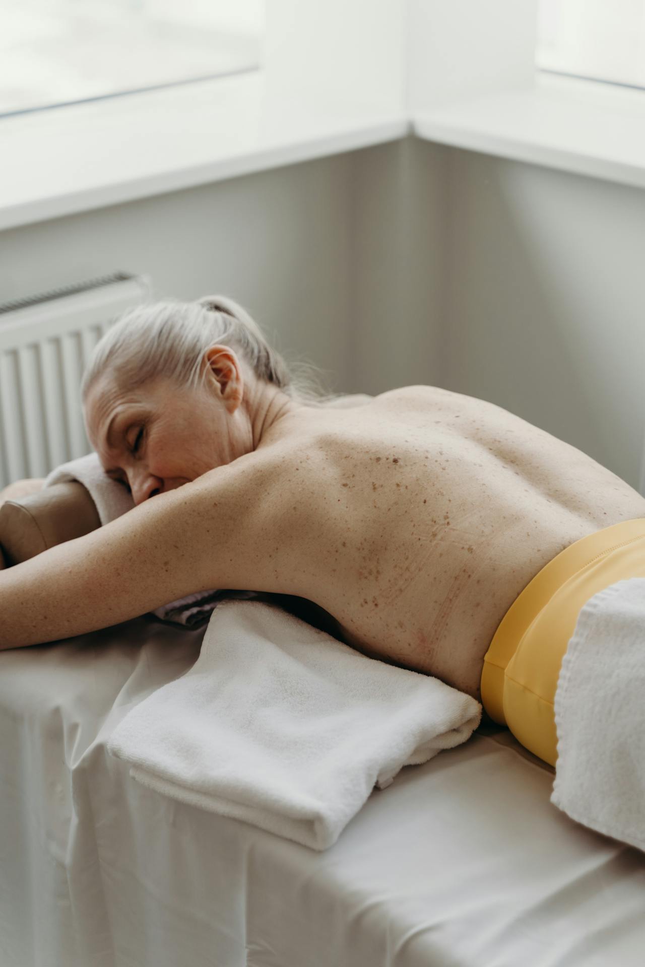 Older woman lying on a massage table as she prepares her body for a TENS Unit treatment.